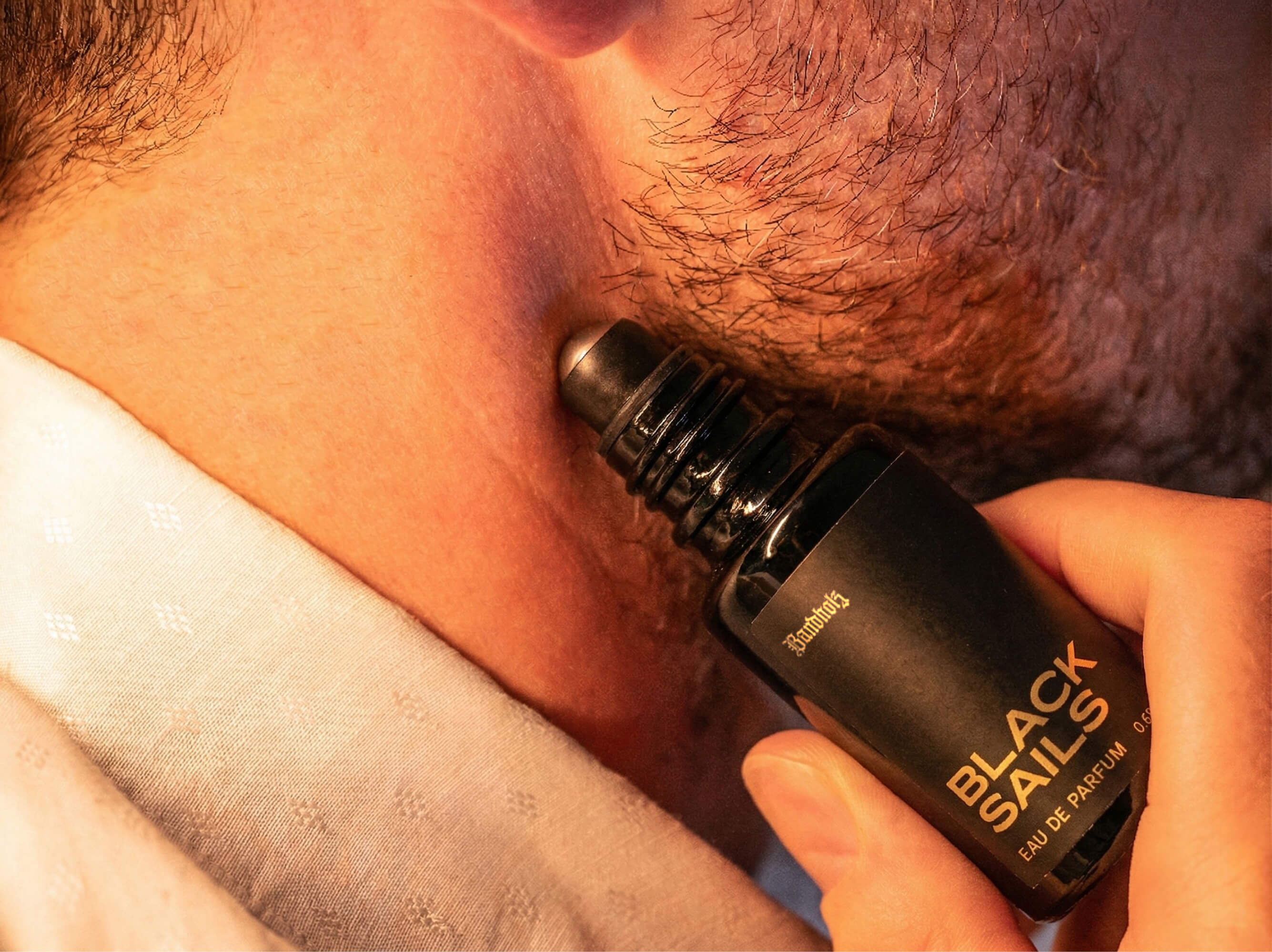 Close-up of stubbled lower face with Bandholz Black Sails Eau de Parfum roll-on bottle held against the skin.
