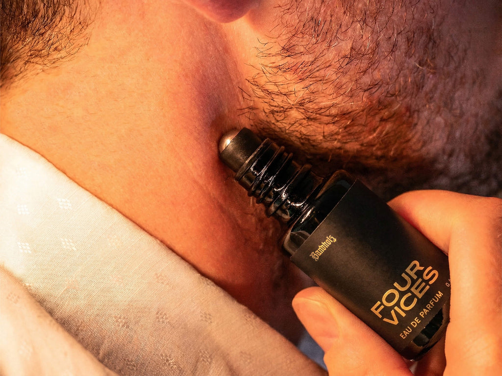 Close-up of stubbled lower face with Bandholz Four Vices Eau de Parfum roll-on bottle held against the skin.