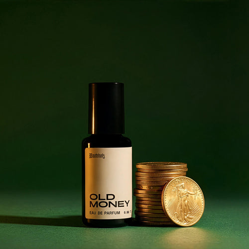 Bandholz Old Money Eau de Parfum bottle beside stacked gold coins on a green background symbolizing the fragrance’s classic refined character.