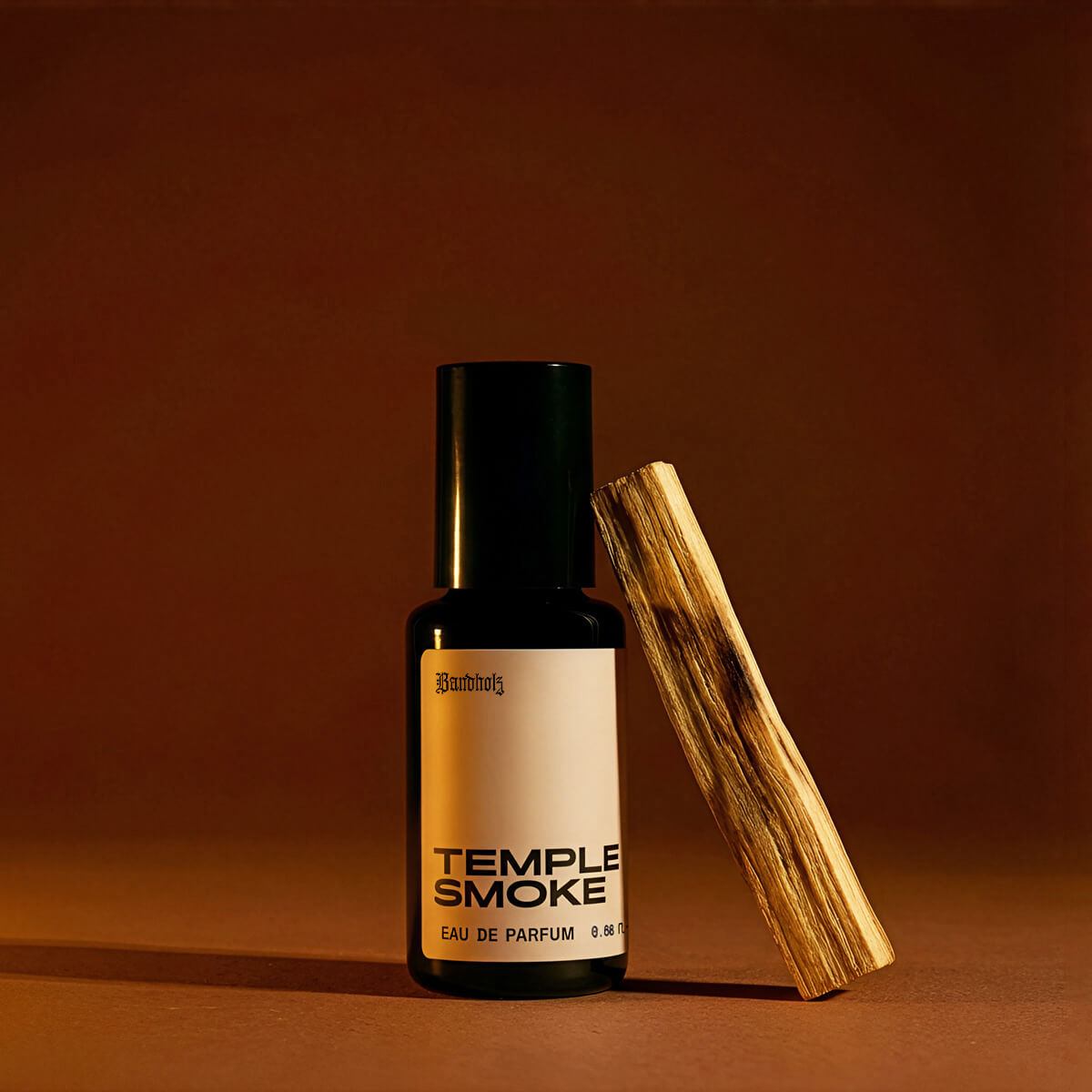 Bandholz Temple Smoke Eau de Parfum bottle with palo santo wood on a warm brown background highlighting the fragrance’s smoky wood scent.