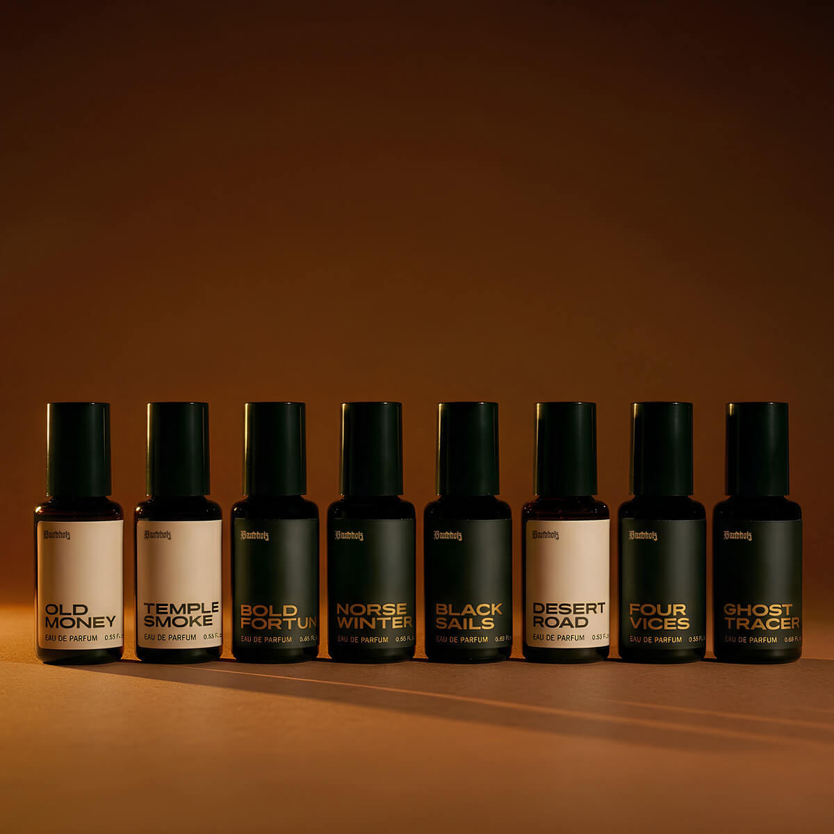 Bandholz Eau de Parfum lineup featuring Old Money, Temple Smoke, Bold Fortune, Norse Winter, Black Sails, Desert Road, Four Vices and Ghost Tracer bottles on a warm amber background.