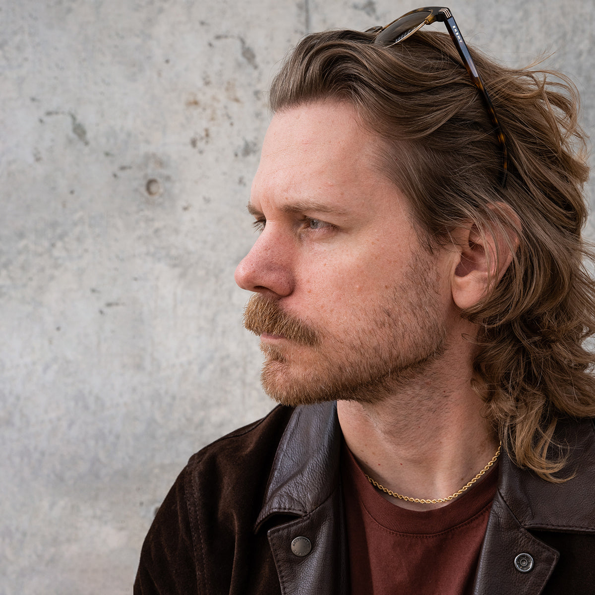 Founder, Eric Bandholz, with long hair and beard wearing sunglasses on his head, standing against a textured wall.